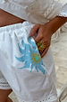 Deloris Sun Ring in gold brass with colourful semi-precious stones, worn on a hand tucked into white printed shorts.