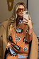 Thumbnail for Tan Sun Copenhagen Jumper featuring sun and swirl motifs, styled with a trench coat and orange sunglasses.