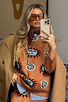 Tan Sun Copenhagen Jumper featuring sun and swirl motifs, styled with a trench coat and orange sunglasses.