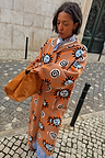 Tan Sun Cardigan with hand-painted sun motifs and dropped shoulders, styled on a cobblestone street.