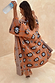 Oversized Tan Sun Cardigan featuring hand-painted Mediterranean sun motifs and wide sleeves in an outdoor setting.