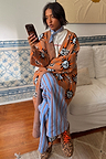 Tan Sun Cardigan with hand-painted sun motifs and an oversized fit, paired with blue striped trousers.