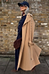 Tan Trench Coat with gold studs on the sleeve, styled with a navy cap and burgundy neck scarf.