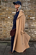 Tan Trench Coat with gold studs on the sleeve, styled with a navy cap and burgundy neck scarf.