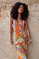 Dolce Vita Valeria slip midi dress with sun motifs and patchwork in orange and blue, shown on a model against a wall.