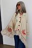 Cream Western Knitted Cape with colourful motifs, button-up front and a long fringed hem on a model.
