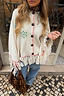 Cream Western Knitted Cape featuring green motifs, black buttons and a fringed hem, styled with denim jeans.