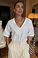 White cotton T-shirt with shoulder pads and a deep V-neck, featuring a boxy fit and styled with yellow striped trousers.