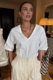 White cotton T-shirt with shoulder pads and a deep V-neck, featuring a boxy fit and styled with yellow striped trousers.