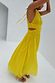 Yellow Ella Dress featuring pleated fabric, side cut-outs and a flowy midaxi silhouette against a white wall.