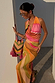 Multicoloured Abstract Beaded Fringe Bag with pink tassels, held by a model wearing a matching print maxi dress.