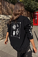 Oversized black sweatshirt with ecru sun and snake embroidery, styled in a London setting with a red phone box.