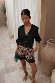 Black Miley Shirt with blouson sleeves and tortoise buttons, styled with lace-trim leopard print shorts in a patio.