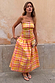 Check Lola Mid-axi Dress in yellow, pink and orange with a ruched bodice and cotton skirt against a rustic wall.