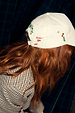 Cream Choose Love Cap featuring embroidered hearts and lips, styled on a model with long red hair in a checked blazer.