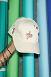 Cream Choose Love Cap with red 'I Choose Love' embroidery and playful motifs held against colourful paper rolls.