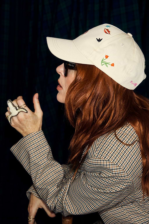 Cream Choose Love Cap with colourful embroidered icons, worn by a red-haired woman in a checkered blazer.