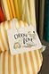 Choose Love Tote Bag in cream recycled cotton with colourful graphic prints, resting on a yellow striped armchair.