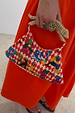 Red checkered Cirque Bag featuring hand-embroidered beads and a tiger-shaped wooden handle, held against an orange dress.