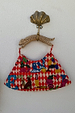 Cirque Bag with red chequered print and hand-embroidered beaded motifs, hanging by its carved wooden leopard handle.