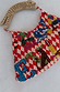 Cirque Bag with red checkered print, hand-embroidered glass bead animal and alphabet motifs and a carved wooden handle.