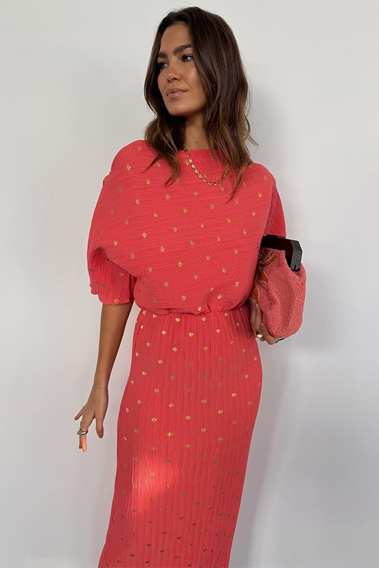 Coral Plisse Tilly Dress featuring gold flecks, an off-the-shoulder neckline and elasticated waist, styled with a pink clutch.