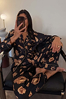 Black Deloris Button Through Pyjamas with gold hand, heart and eye motifs, worn by a model in a mirror selfie.