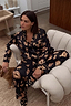 Black Deloris Button Through Pyjamas with iconic gold hand and heart motifs, shown on a model lounging at home.