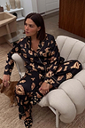 Black Deloris Button Through Pyjamas with iconic gold hand and heart motifs, shown on a model lounging at home.
