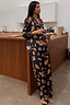 Black Deloris Button Through Pyjamas with iconic gold hand and heart motifs, shown on a model in a kitchen.