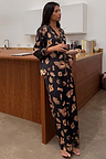 Black Deloris Button Through Pyjamas with iconic gold hand and heart motifs, shown on a model in a kitchen.