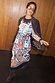 Geometric Gaia Dress in a multi-coloured plisse fabric, styled with a brown blazer and pointed boots.