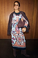 Geometric Gaia Dress featuring abstract motifs on pleated plisse fabric, styled with a brown jacket.