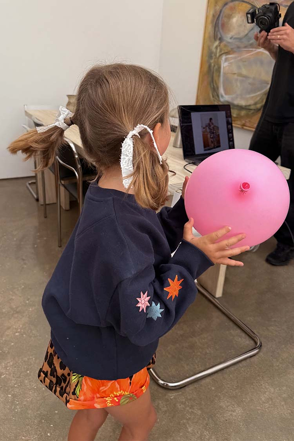 Kids Navy Charms Sweatshirt with colorful sun and star sleeve embroidery, worn by a child holding a pink balloon.