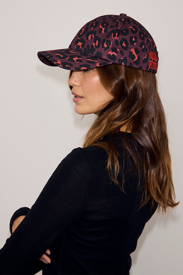 Dark Leopard Cap featuring an iconic burgundy animal print, worn with a black top for a casual look.