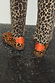 Leopard Pony Trainer in iconic leopard print leather with contrast orange heel tabs, worn with leopard trousers.