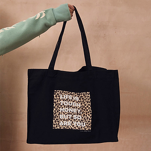 Black canvas tote bag with the leopard print slogan Life Is Tough Honey, But So Are You, held by a hand.
