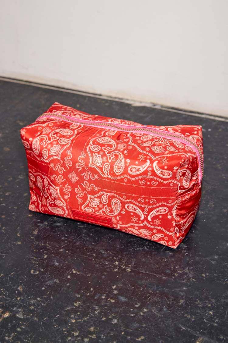 Red bandana print makeup bag featuring a reversible paisley design and pink zip closure.