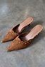Tan suede Scallop City Mules with gold stud detailing and scalloped edges on a grey stone floor.