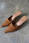 Tan suede Scallop City Mules with gold stud detailing and scalloped edges on a grey stone floor.