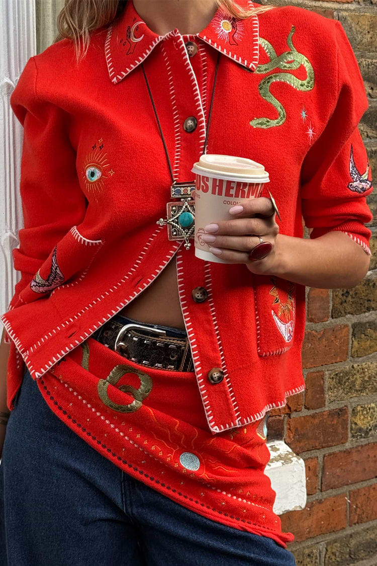 Red Mystical Cardigan with jacquard motifs and blanket stitch detailing, paired with blue jeans.