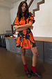 Black Poppy Mini Nara Dress featuring an orange poppy print, shirred front and pleated skirt on a model.
