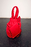 Thumbnail for Red Velvet Bow Bag with an oversized bow detail and padded top handle, set against a dark textured floor.