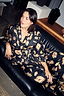 Deloris Satin Robe and pyjama trousers with iconic gold motifs, styled for lounging on a leather sofa.