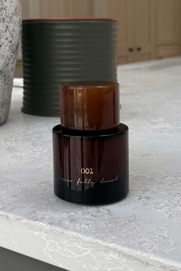 NFD Eau De Parfum 001 in a dark amber glass bottle with a tortoiseshell cap on a white marble surface.