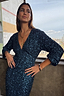 Teal Sequin Emma Dress featuring a V-neckline and long elasticated sleeves, worn by a model by a window.