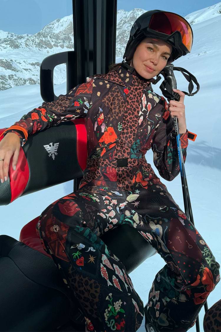 Night Garden Ski Suit with leopard and poppy motifs, shown on a model in a ski lift holding ski poles.