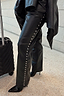 Thumbnail for Black vegan leather studded leg trousers featuring silver side studs, styled with a suitcase for a vacation.
