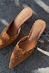Tan Suede Scallop City Mules with gold studs and scalloped edges, shown in a top-down view on a textured surface.