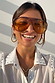 Orange Acetate Visor Sunglasses on a smiling model with 70s-inspired tinted lenses and gold hoop earrings.